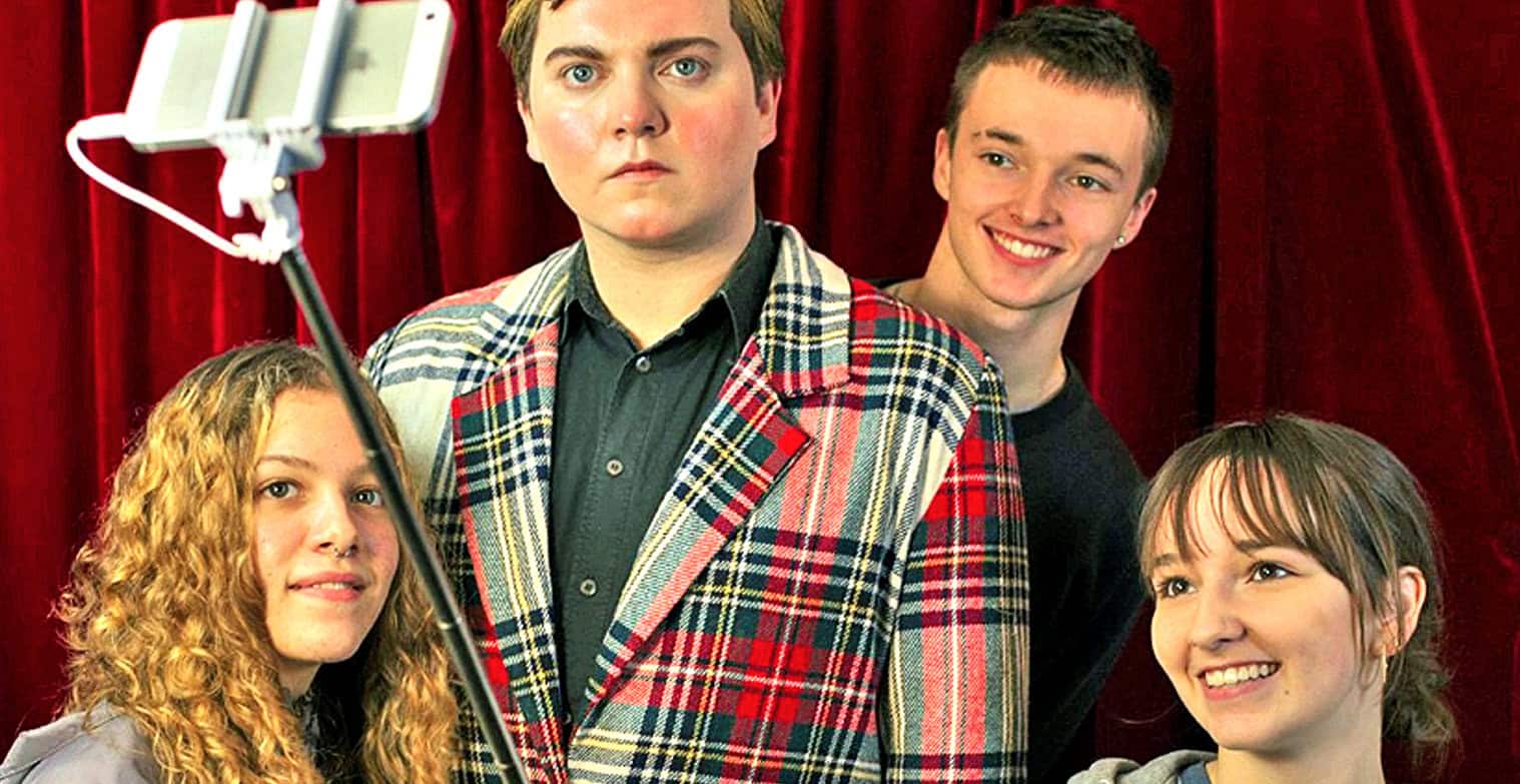 Young adults taking a group selfie with a selfie stick in front of a red curtain, capturing a fun moment at an event or gathering, showcasing friendship and modern photography.