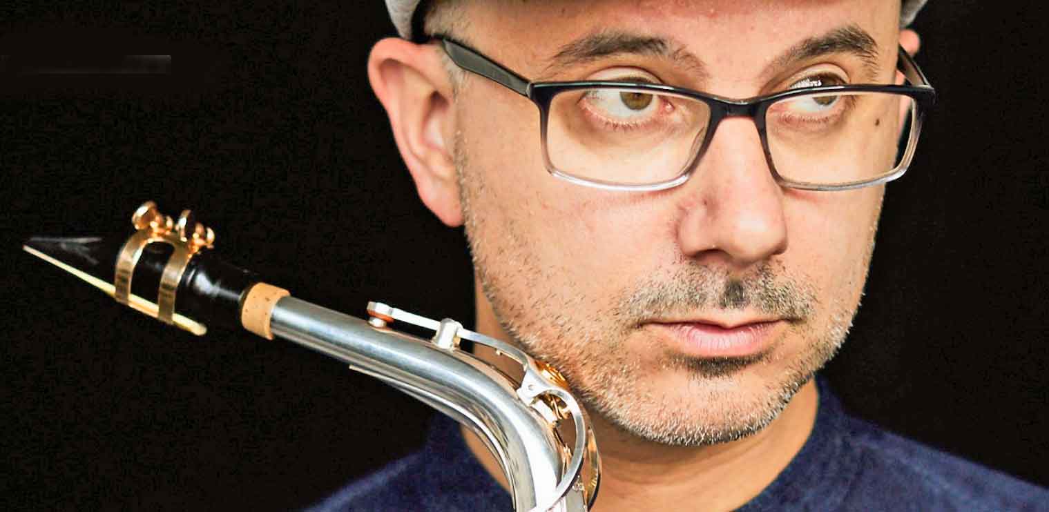 Close-up of male jazz musician with glasses holding a silver and gold clarinet, focusing on his intense expression, showcasing the artistry and passion for music, in a studio setting.