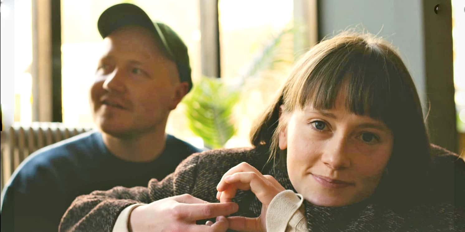 Young woman and man sitting indoors, enjoying music and conversation, capturing nostalgic moments at Past Daily sound archive.