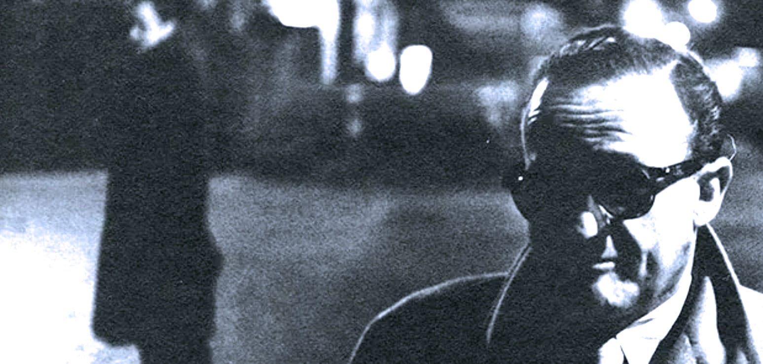 Vintage black and white photo of a man with sunglasses listening to music or news, representing historical audio recordings from the Past Daily sound archive.