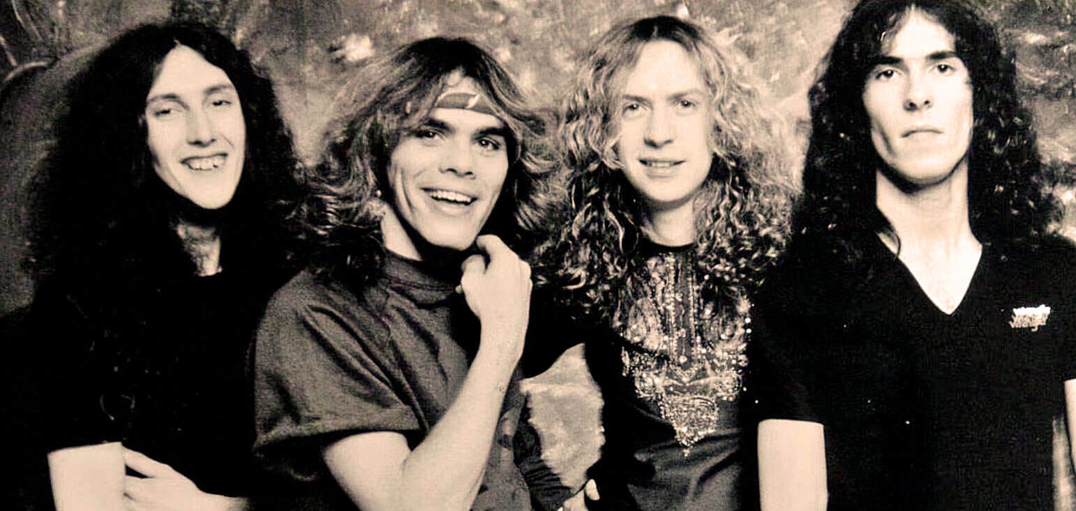 1970s rock band photo with long hair, vintage style, black and white image, band members smiling and posing casually, classic rock music scene.