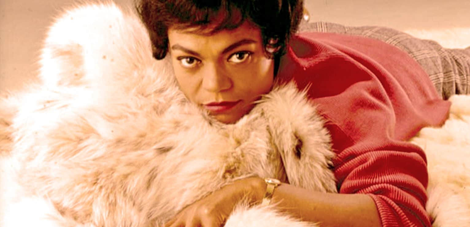 Elegant woman with short hair lying on a luxurious fur coat, wearing a red sweater, embodying vintage fashion style.