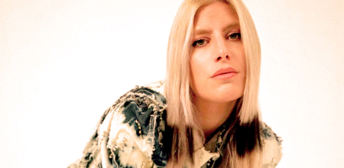 Blonde woman with a serious expression wearing a patterned jacket, promoting the Past Daily sound archive of news, history, and music. Perfect for historical audio recordings, interviews, and vintage radio content.