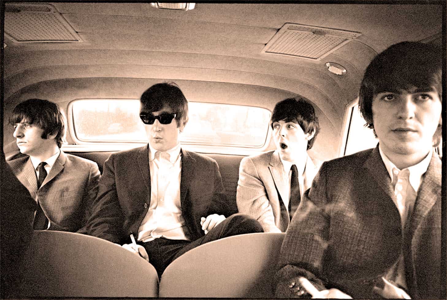 Vintage band of four young men, dressed in 1960s suits, traveling in the backseat of a classic car, highlighting music history and era-specific fashion, perfect for a nostalgic sound archive image.
