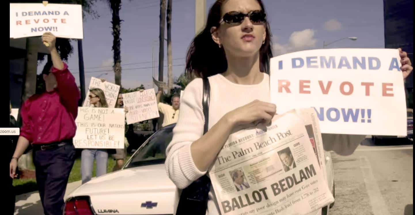 Protesters holding signs and a newspaper during a political demonstration for voting rights and civic activism at a street rally.