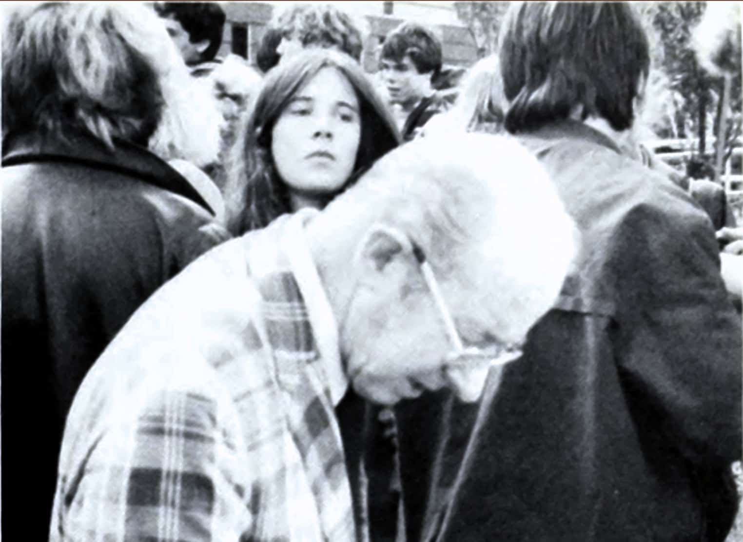 People gathered outdoors, some engrossed in conversations, capturing a moment in a historic or newsworthy event. The black-and-white image emphasizes a historical context, possibly related to music, news, or social movements.