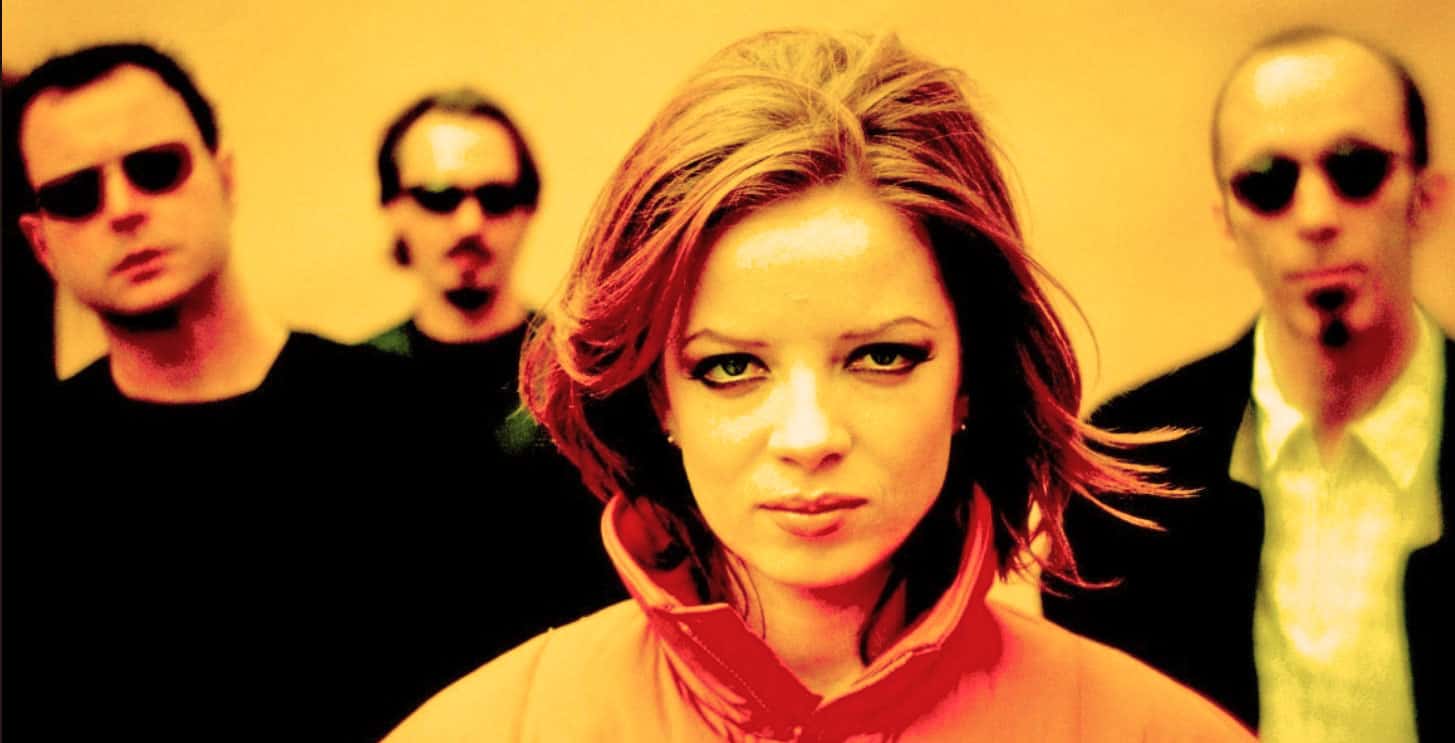 Red-haired woman with intense expression, accompanied by three men in sunglasses, representing music and pop culture, capturing a vibrant, energetic scene from the past daily sound archive.