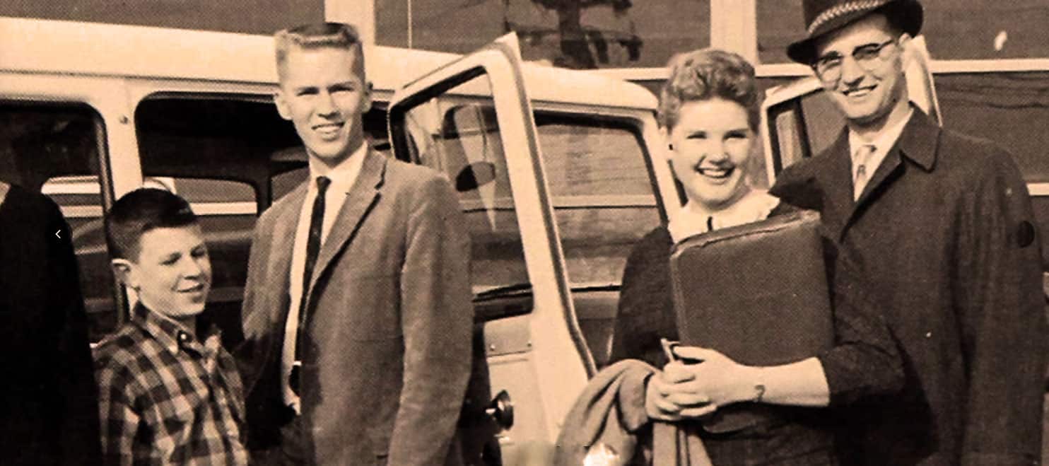 A vintage black and white photo of four smiling people standing next to a truck, representing historical news, music, and life moments from past decades.