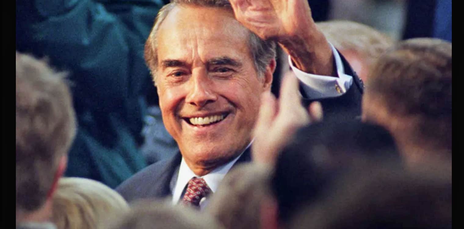 Smiling man in suit at political or social event, surrounded by crowd, capturing a moment of celebration or recognition.