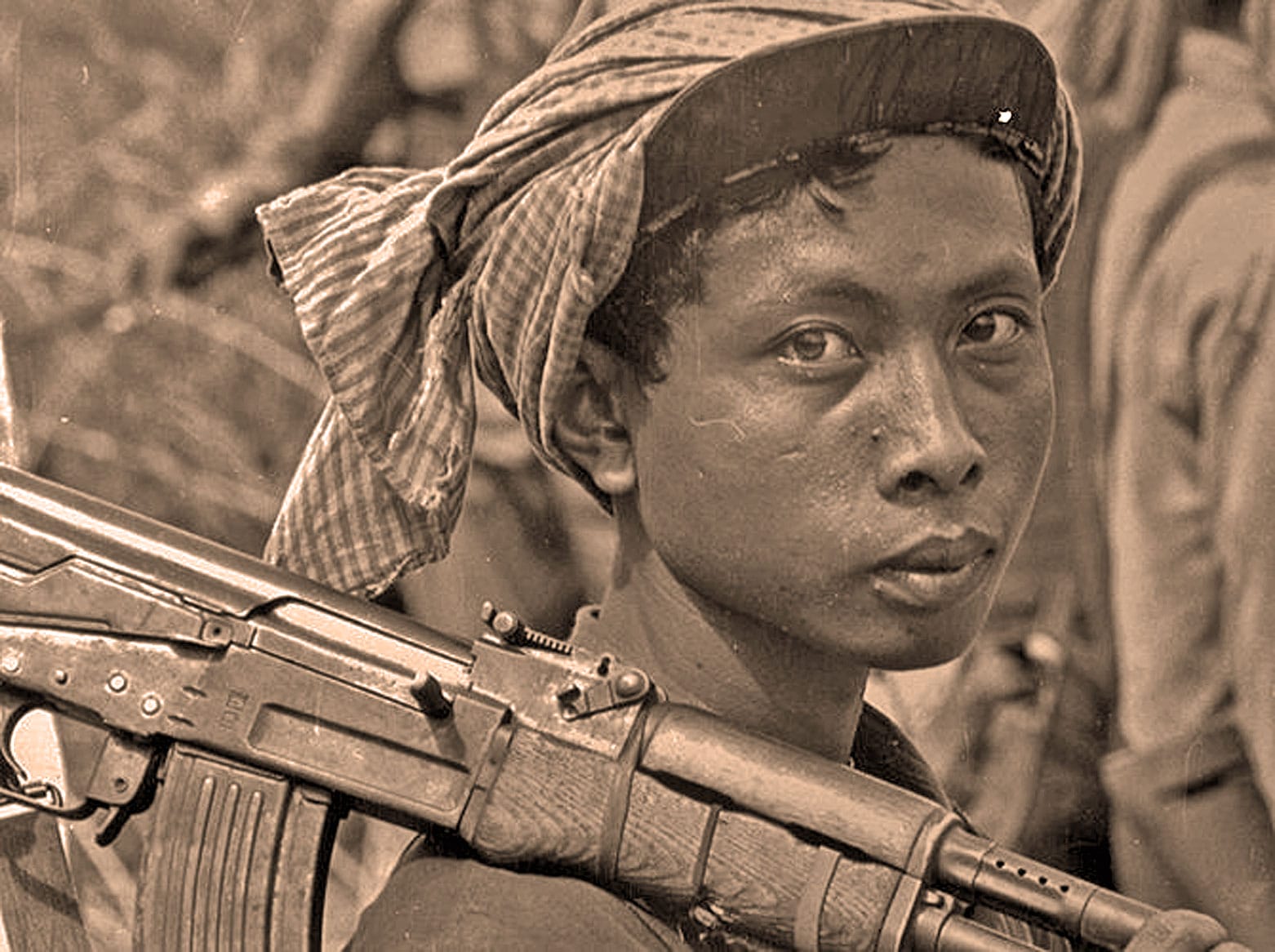 Young woman soldier wearing a headscarf, holding a rifle, in a historical or documentary photo related to conflict or war, featured on Past Daily's sound archive of news, history, and music.