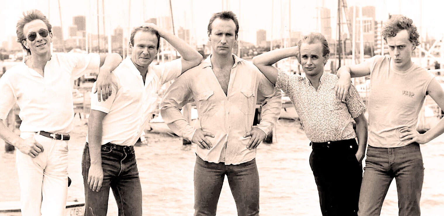 Vintage black-and-white photo of The Beatles members standing outdoors with a cityscape background, showcasing iconic 1960s music history and legendary rock band.