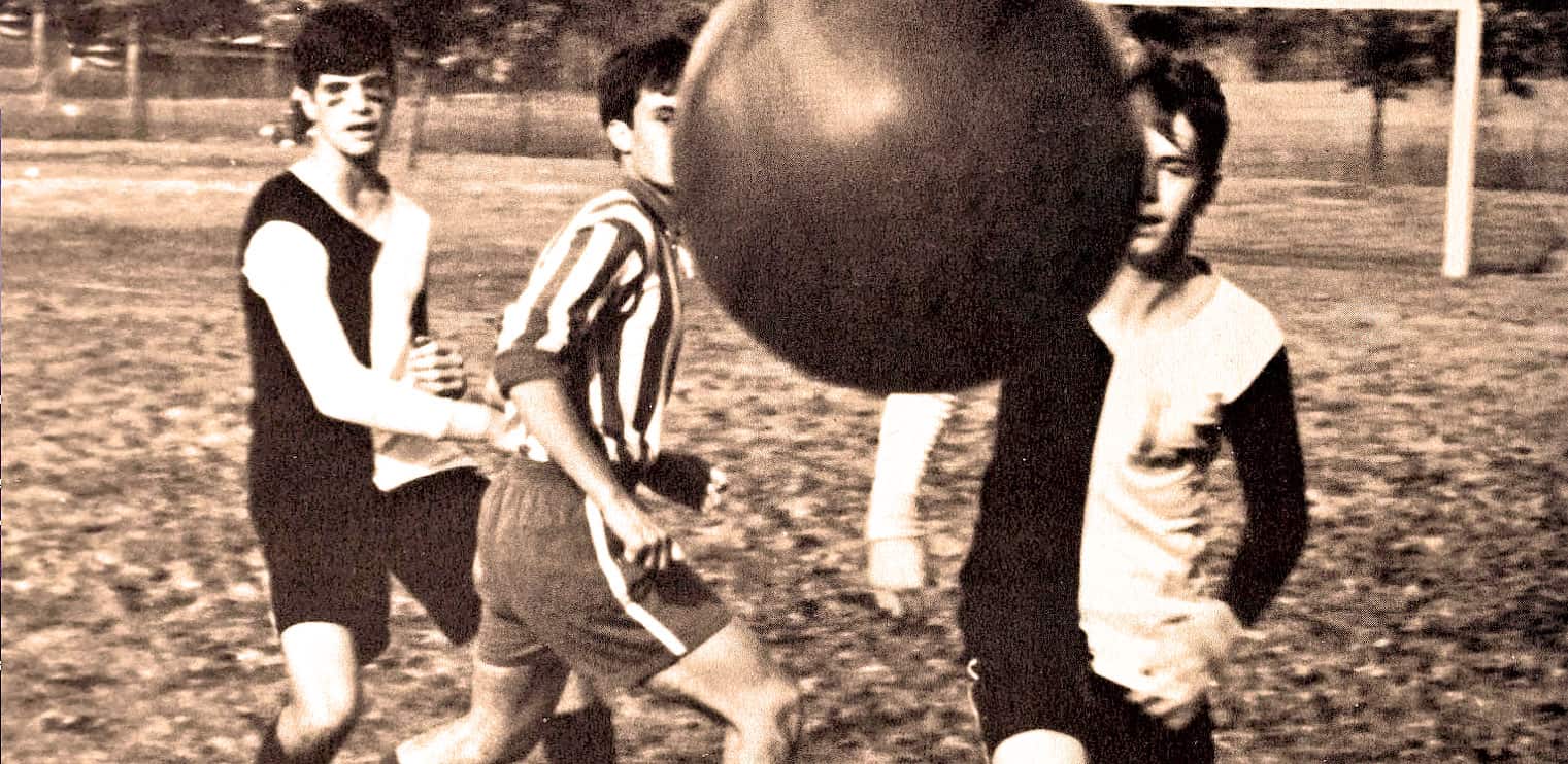 A sepia-toned photo of young boys playing soccer in a park, showcasing nostalgic sports moments with vintage attire and a soccer ball, emphasizing historical sports archive content.