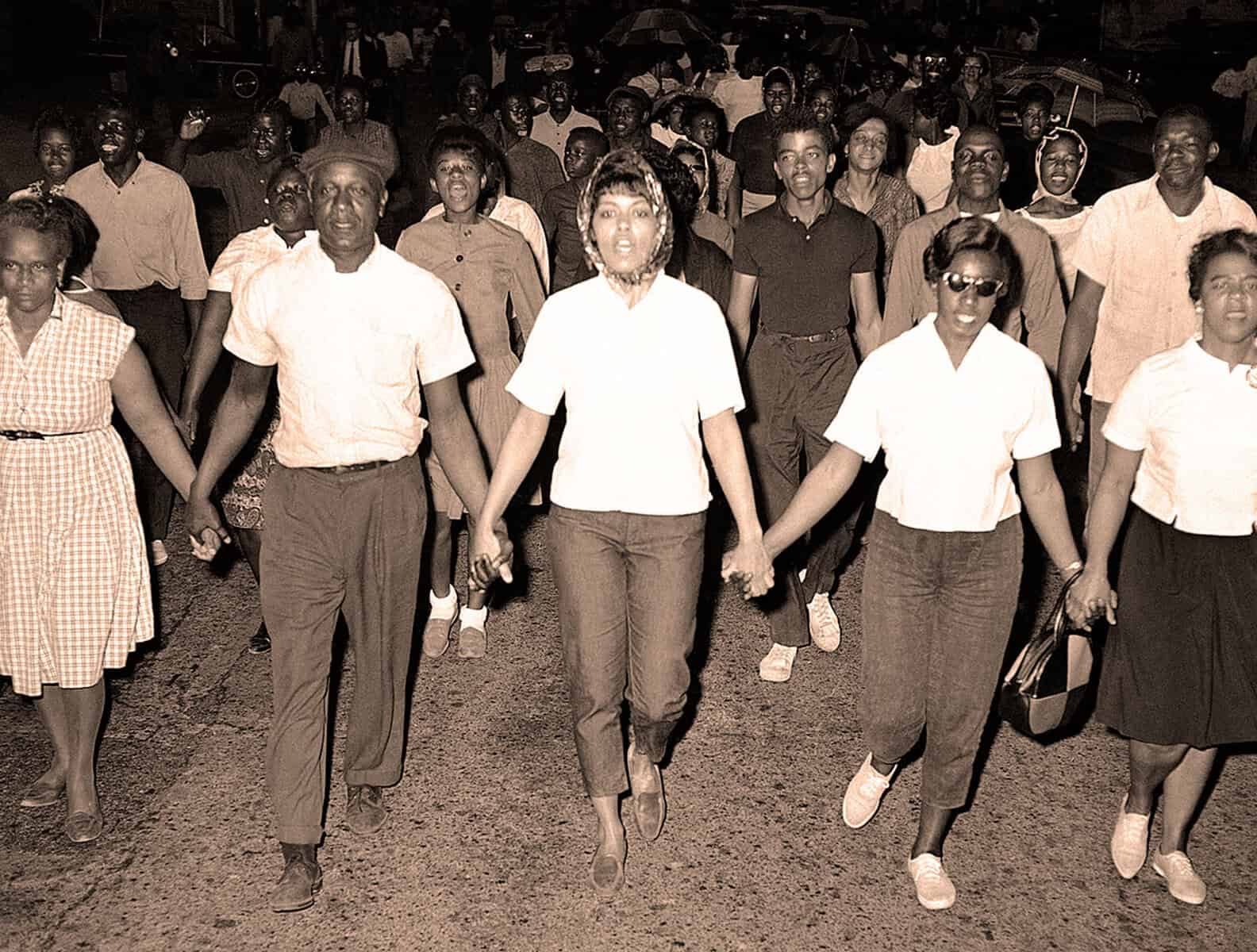 People participating in a historical protest or march in Africa, holding hands and walking together at night, capturing a moment of social activism and community unity.