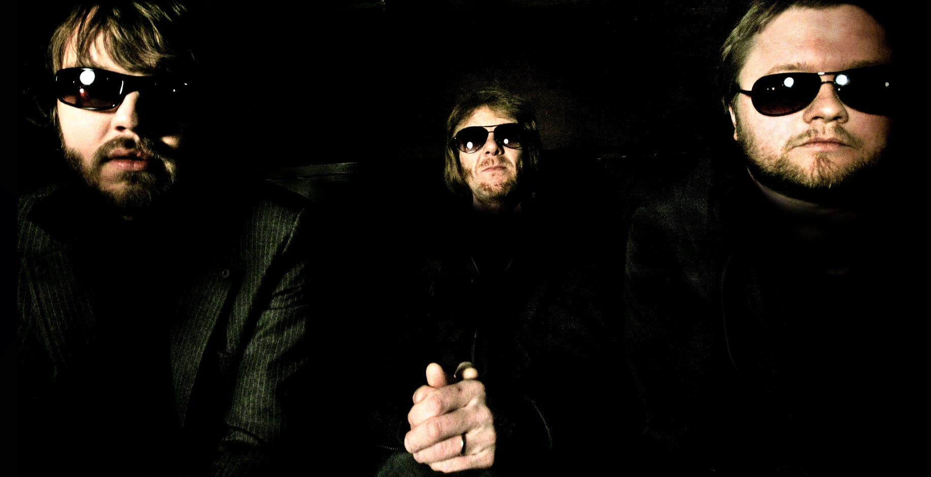Vintage rock band members with sunglasses in a dark setting, emphasizing music history and classic rock era.
