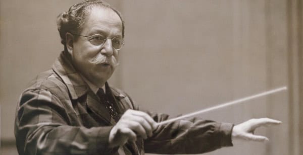 Conductor leading an orchestra with baton, focusing on music history and archival recordings.