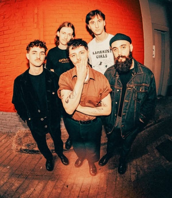 A sound archive of news, history, and music featuring a band of five young musicians standing against a red brick wall, capturing the essence of vintage and indie music culture.