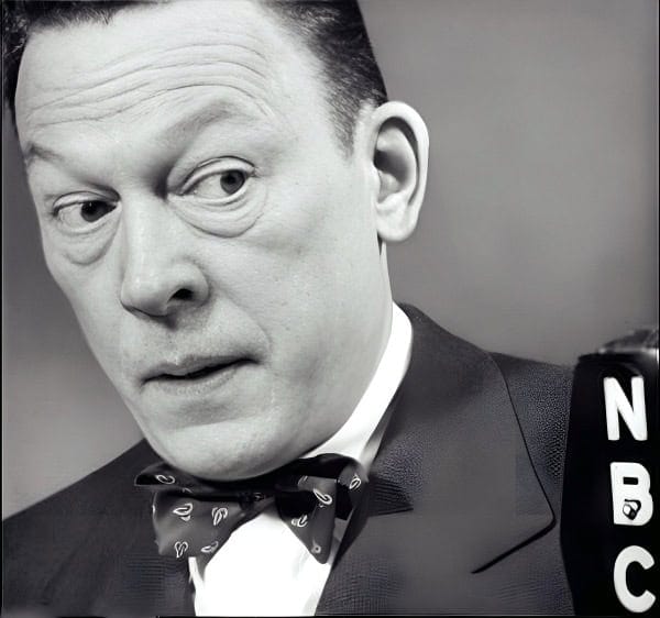 Unfocused black and white image of a man in a suit and bow tie, speaking into a microphone with the NBC logo, capturing a news broadcast or historical moment recalling classic media coverage.