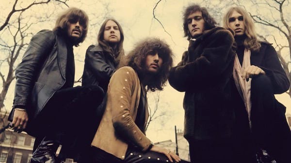 Vintage rock band outdoor photoshoot with overcast sky, emphasizing classic 70s music style, edgy fashion, and atmospheric setting.