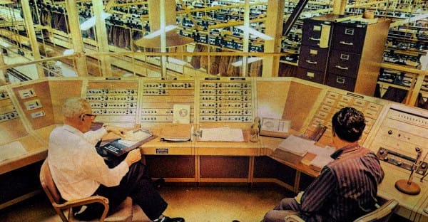Vintage radio broadcasting studio with two technicians monitoring news and music recordings, showcasing a historic sound archive setting.