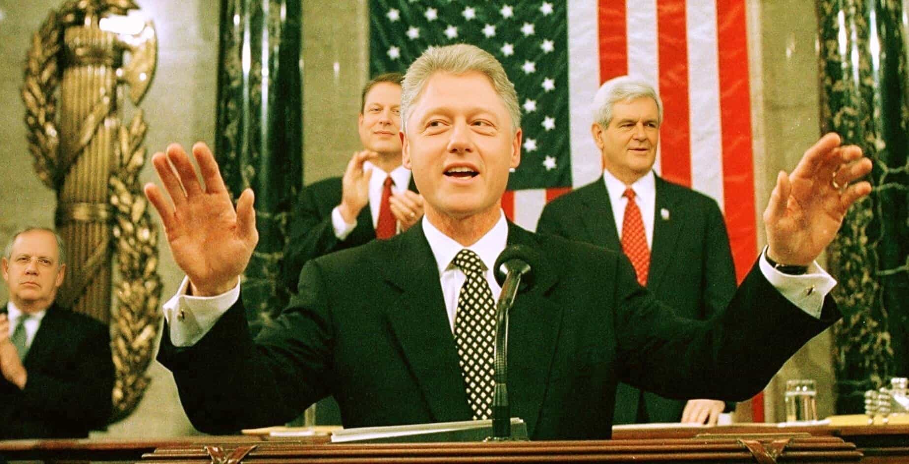 Official during a historic political speech, US flag backdrop, formal suit, presidential address, American politics, government leaders, televised speech, past daily news archive, history and music documentation.