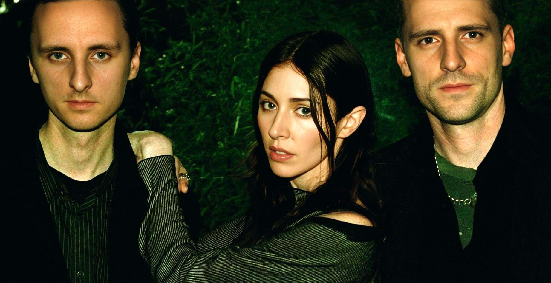 Vintage rock band promotional photo, featuring three musicians with a dark lush green background, highlighting music history and classic band imagery.