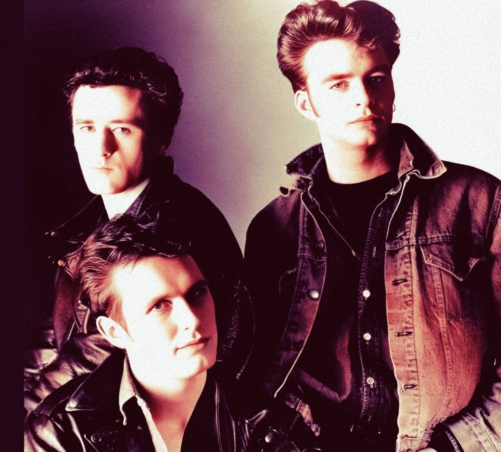 Vintage 1980s rock band portrait, featuring three male band members in leather jackets and denim, representing music history and classic rock era, associated with nostalgic music sound archive.