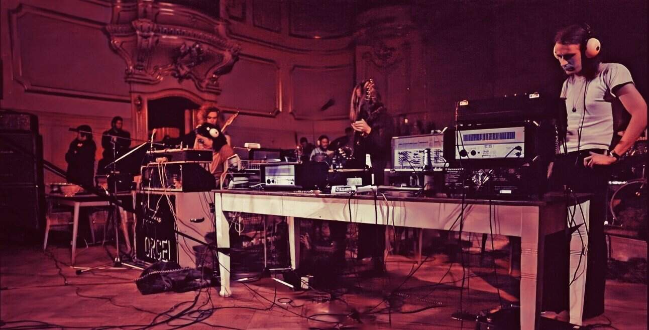 Deep house DJ performance at a live music event with electronic equipment and headphones in an ornate venue with vintage decor.