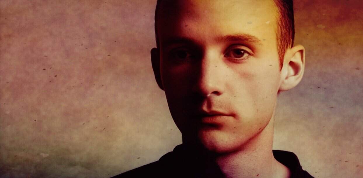 Young boy with fair skin and short hair, contemplative expression, softly lit in warm tones, representing history and youthful innocence.