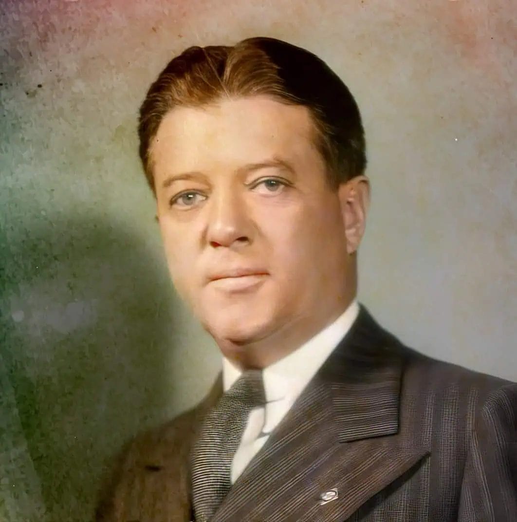 Archive photo of a man with slicked-back hair wearing a pinstripe suit and tie, possibly a historical figure or from a classic TV show, suitable for a nostalgic news or history archive website.