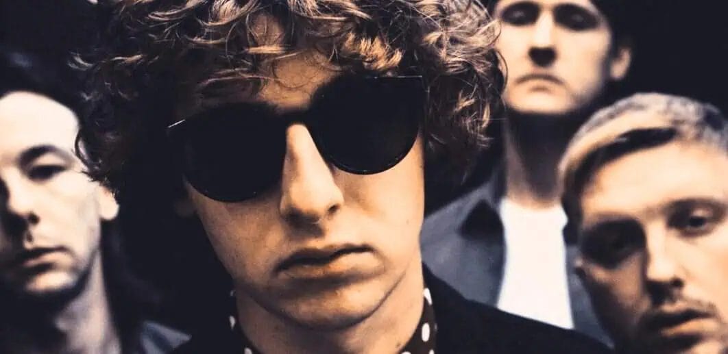 Vintage black-and-white photograph of The Beatles, showcasing John Lennon wearing dark sunglasses and iconic hairstyles, capturing a classic moment in music history.